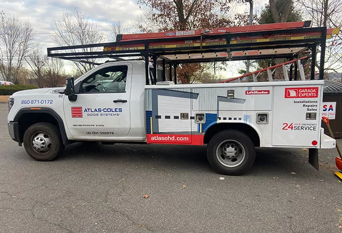 Service truck with Atlas-Coles Door Systems branding, ladders, and emergency contact info, parked on a paved surface.